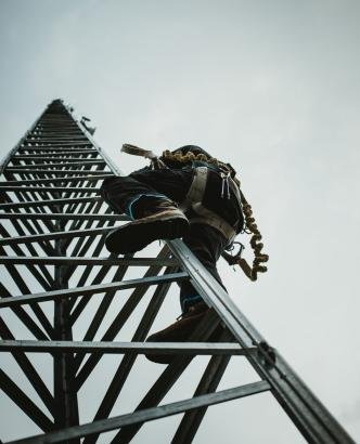 Telecom Worker Climbing Antenna Tower with Tools and Harness